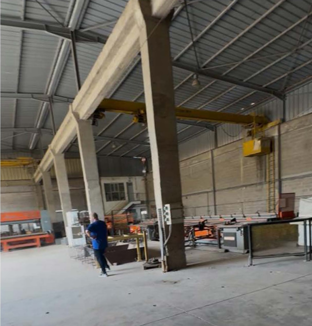 Atelier de façonnage d’acier : poteaux béton, pont roulant jaune, charpente métallique